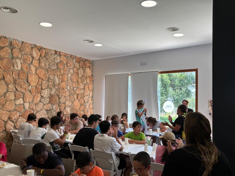 Los participantes en el campamento aplauden mientras la cumpleañera está de pie ataviada con una corona y una banda.