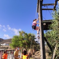 Niña haciendo escalada mientras es guiada y ayudada por los monitores