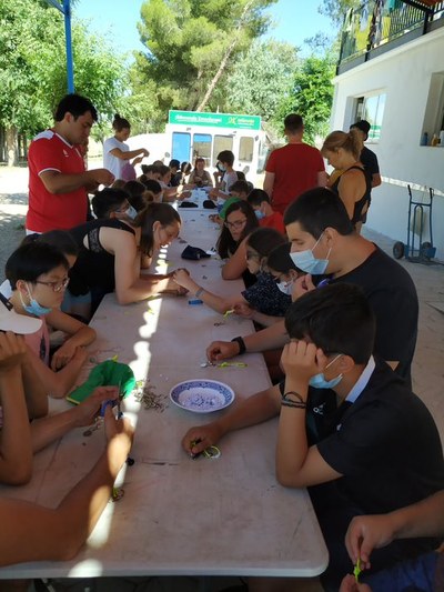 Taller de llaveros: varios niños sentados a una mesa alargada elaboran llaveros con cuerda y cuentas