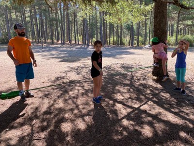 Tres participantes se preparan para subir a una cuerda atada entre dos árboles
