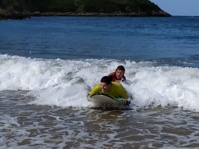 Un monitor y un participante surfean una ola