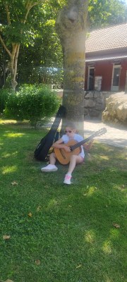 Una participante toca la guitarra sentada al lado de un árbol