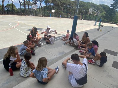 Un grupo de participantes, sentado en círculo, hace estiramientos al lado de la cancha de baloncesto