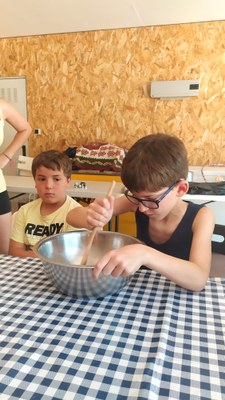 Dos participantes en el taller de cocina, uno de ellos amasando con un bol y una cuchara