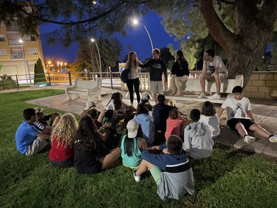 Todos los participantes sentados en el césped escuchan las instrucciones de dos monitores