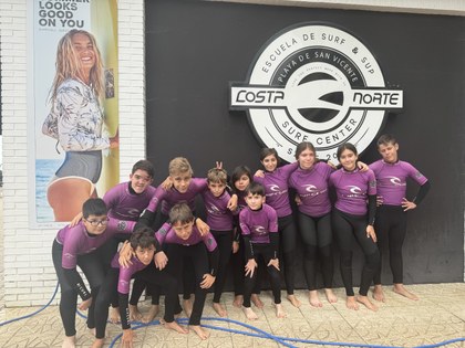 Foto de grupo, todos los campistas vestidos con sus neoprenos preparados para hacer surf.