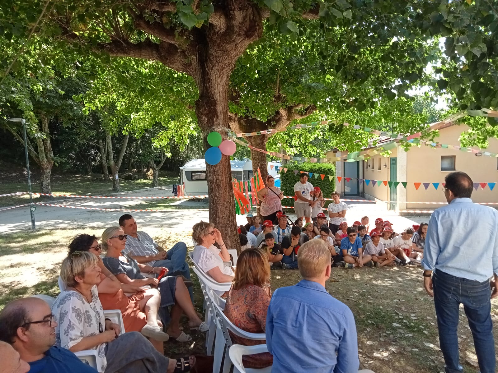 Participantes y visitantes sentados escuchando durante la ceremonia final del campamento. Participantes y visitantes sentados escuchando durante la ceremonia final del campamento.