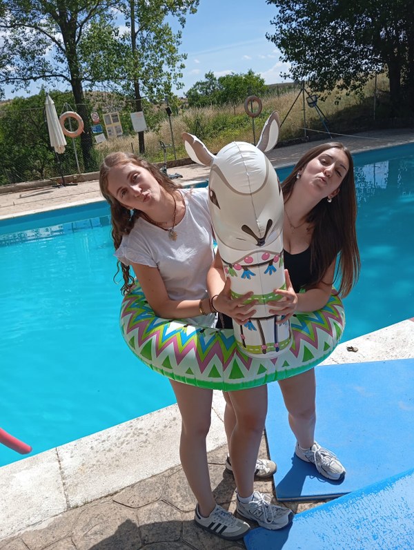 Dos acampadas posando en la piscina con un flotador en forma de alpaca