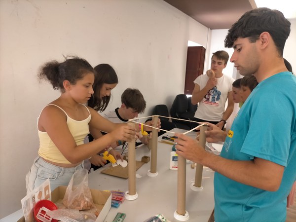 16.18.07.2026.JPG Participantes trabajando en la construcción de un edificio a partir de materiales reciclados, como tapones y tubos de cartón.