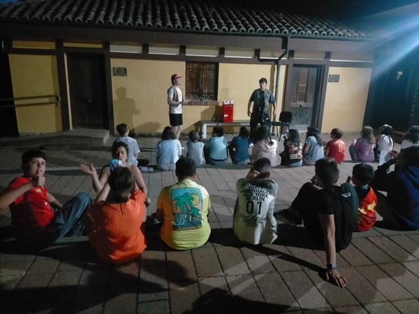 f.20.07.2026.JPG Participantes sentados en el suelo formando dos líneas, en una fotografía nocturna durante la velada.