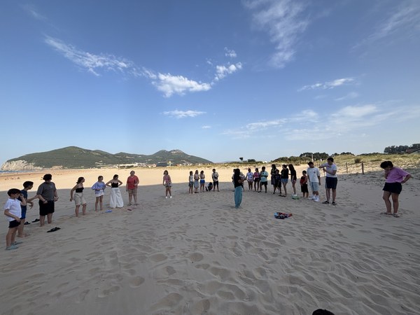 Participantes dispuestos en círculo en la playa escuchando las normas del campamento
