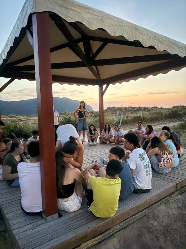 Participantes sentados bajo un cenador de madrea junto a la playa al atardecer