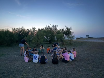 Participantes sentados en el suelo en círculo, al atardecer junto a la playa.