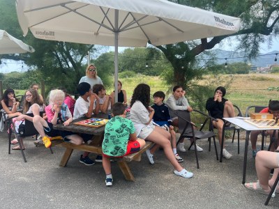 Participantes sentados en mesas tipo picnic bajo una sombrilla jugando al parchís durante el tiempo libre.