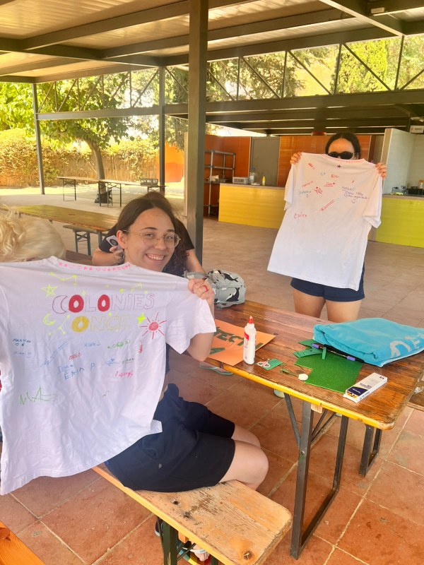 Participantes decorando camisetas blancas con firmas y dibujos de recuerdo del campamento.