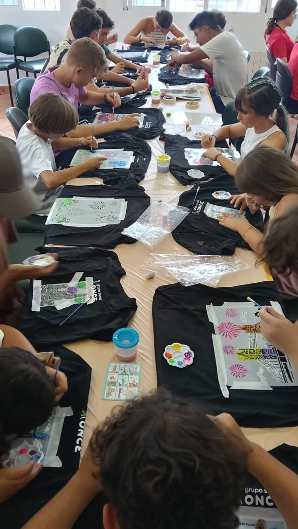 Participantes sentados en una mesa alargada decorando sus camisetas de ONCE con plantillas y pintura en relieve.