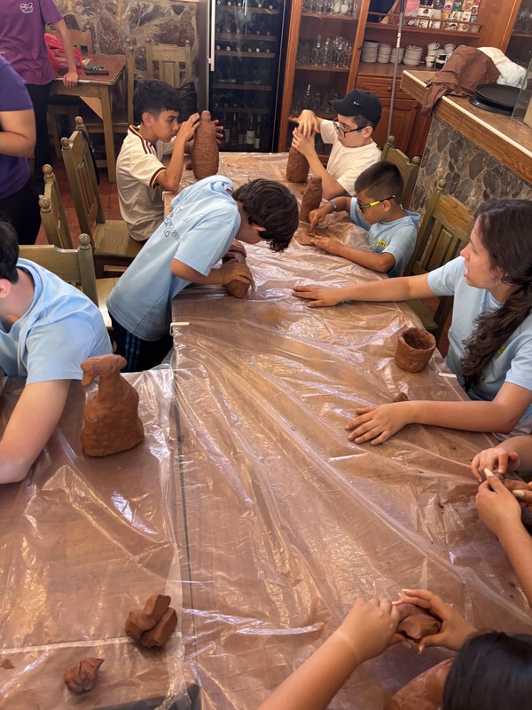 Grupo de participantes durante el taller de barro, sentados en mesas protegidas con plásticos. 